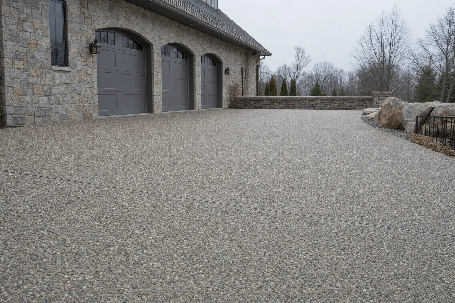 Surface de béton désactivé avec joints de dilatation, devant une maison en pierre.